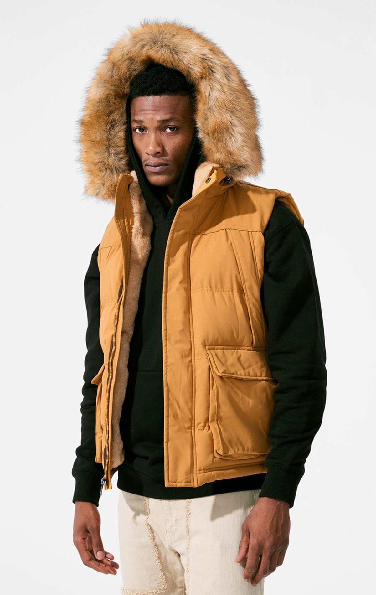 Wheat color Faux fur-lined hooded jacket made of a water-resistant polyester shell featuring a removable hood with a removable faux fox fur trim. The hood and front of the jacket are lined with faux rabbit fur for superior warmth. The jacket has JC branded zippers throughout, dual pockets at the sides with button openings, and a full zipper front opening. Faux suede taping adorns the front zipper.